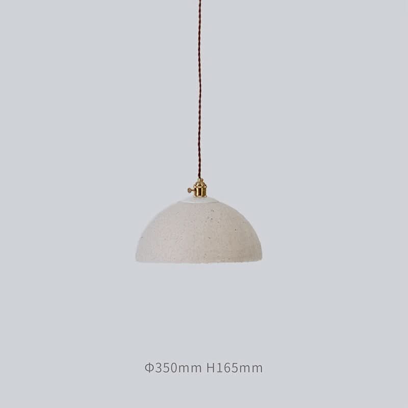 Cream paper mache lamp shade with textured finish and brass hardware, hanging from cord.