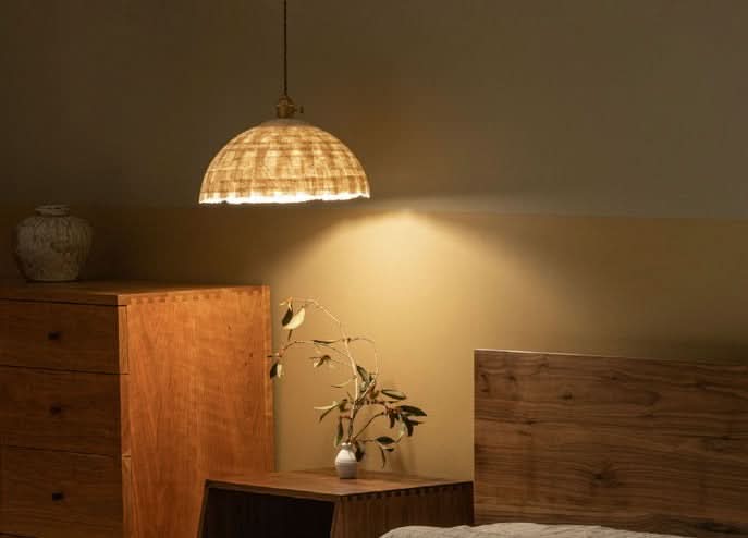 Natural fiber paper mache lamp shade casts warm light over a wooden bedroom.