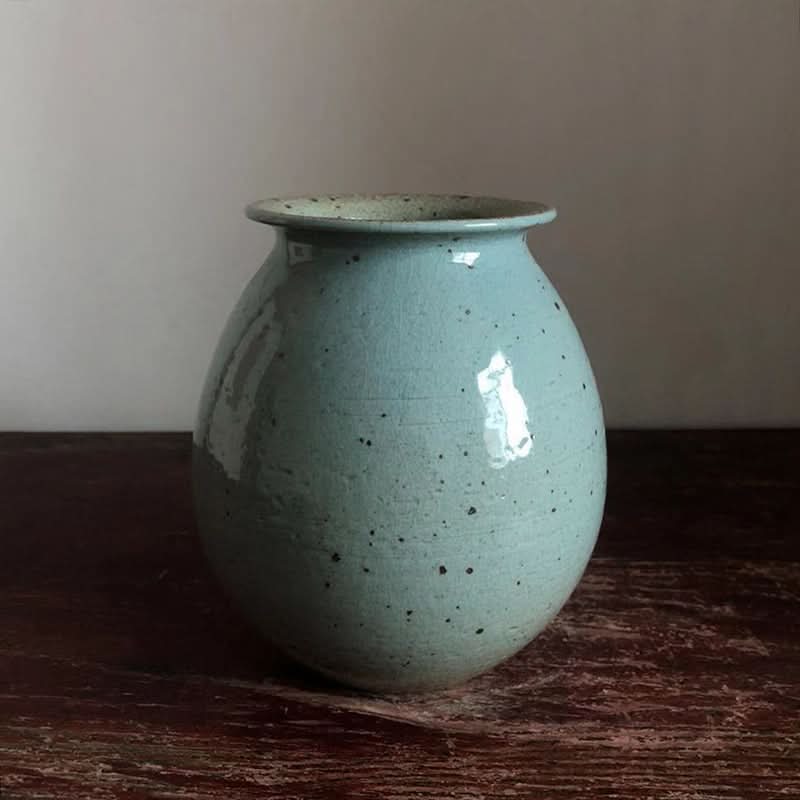 Speckled light blue ceramic vase for flowers on a wooden surface.