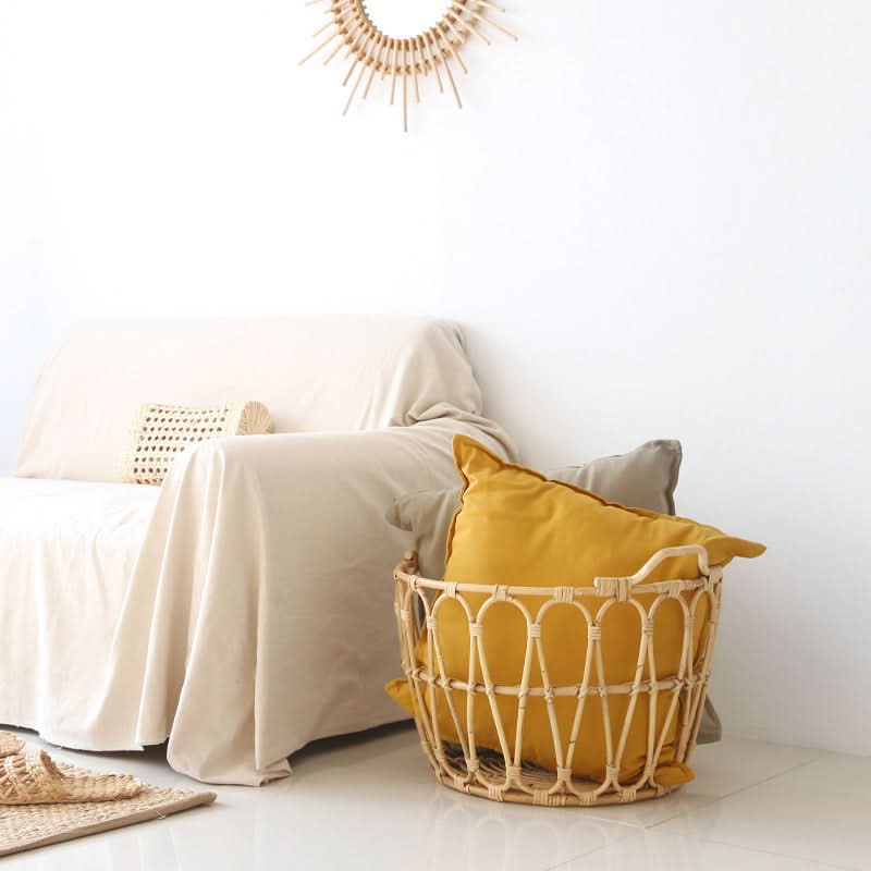 Rattan Round Storage Basket Zig Zag Pattern holding yellow and grey pillows on a white floor beside a cream couch.