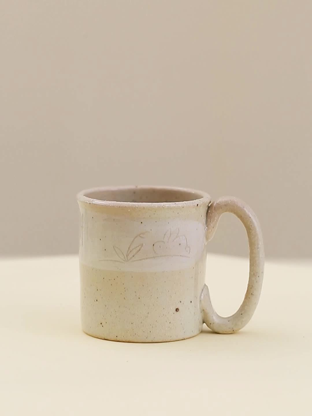 Stoneware Wangu Burning Rabbit Mug Made In Japan, light speckled beige ceramic with etched rabbit design.