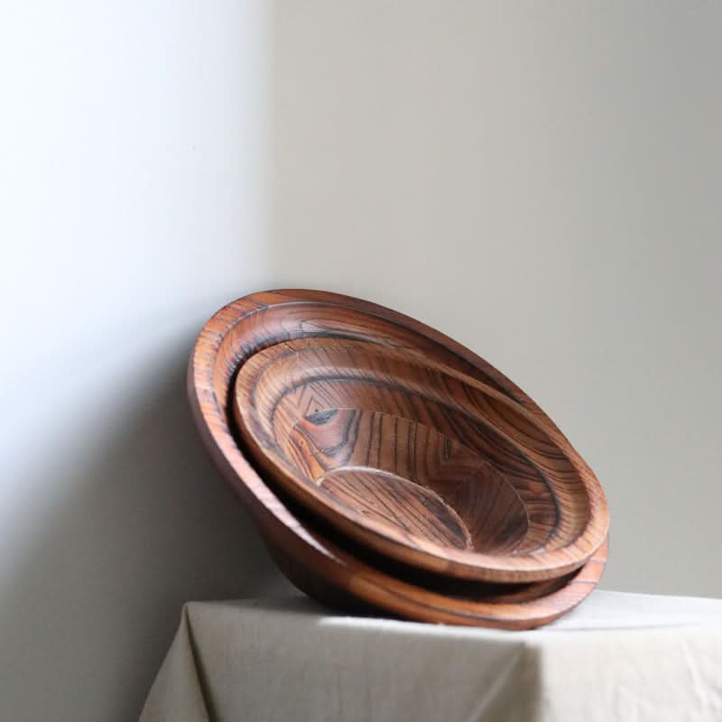 Stack of three handmade retro wooden bowls with visible grain, set on a linen-covered surface.