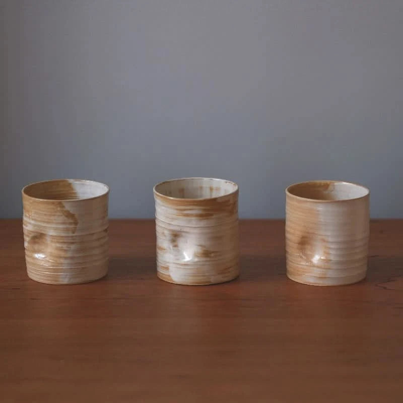 Three handmade ceramic dented coffee cups with brown and white glaze on a wooden surface.