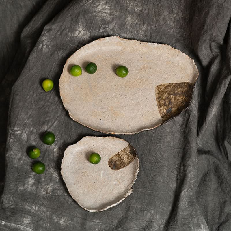 Wabi-sabi irregular beige serving tray with limes on textured dark fabric