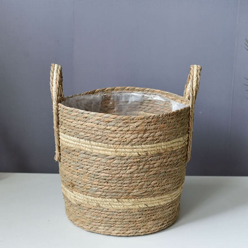 Woven seagrass plant basket with handles and neutral stripes, perfect for home decor.