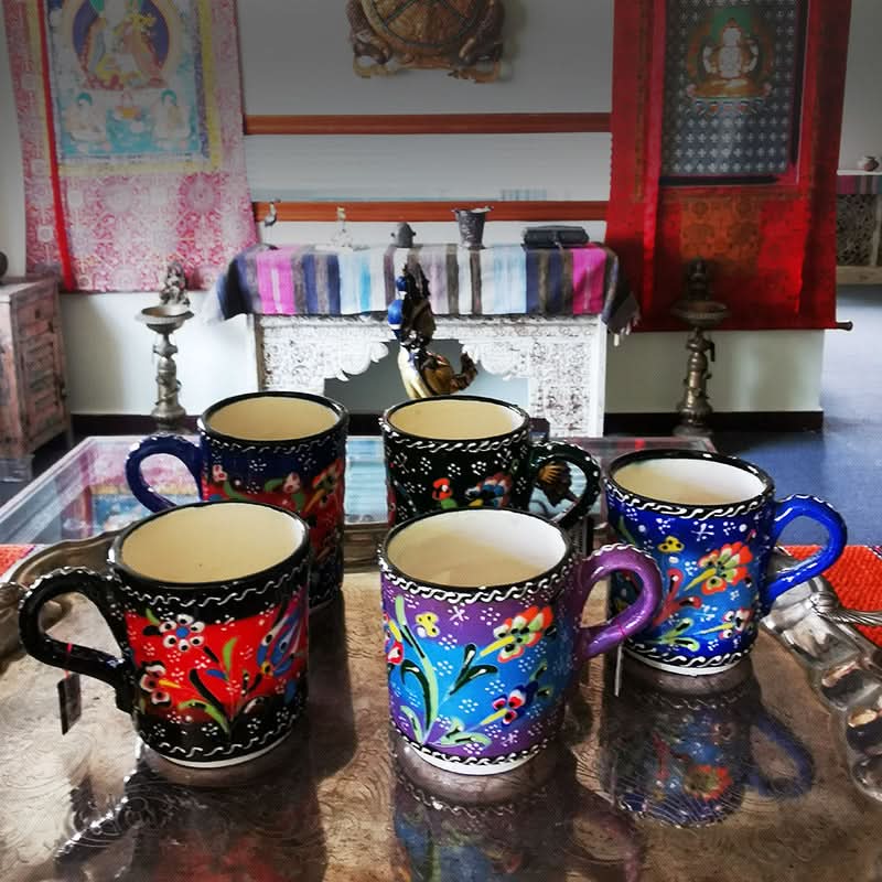 Colorful Turkish glazed ceramic mugs with floral patterns on a decorative tray in a home setting.
