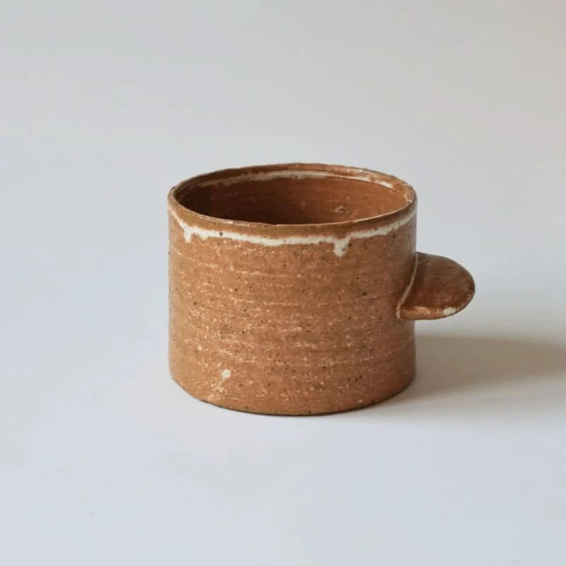 Brown rough pottery ceramic mug with straight handle on white background.