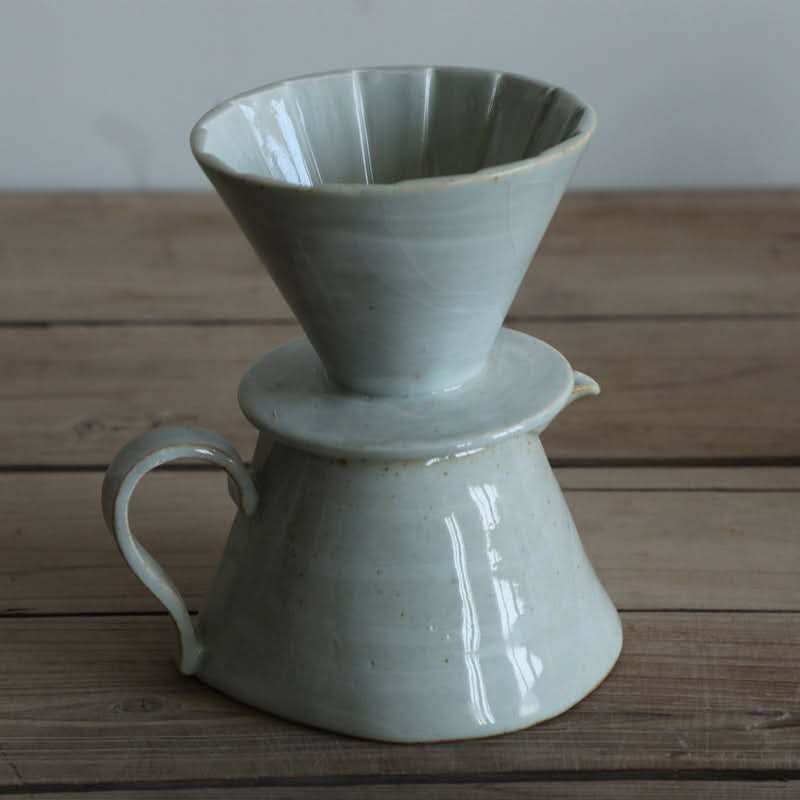 Grey ceramic textile folded style coffee brewer set on a wooden table.