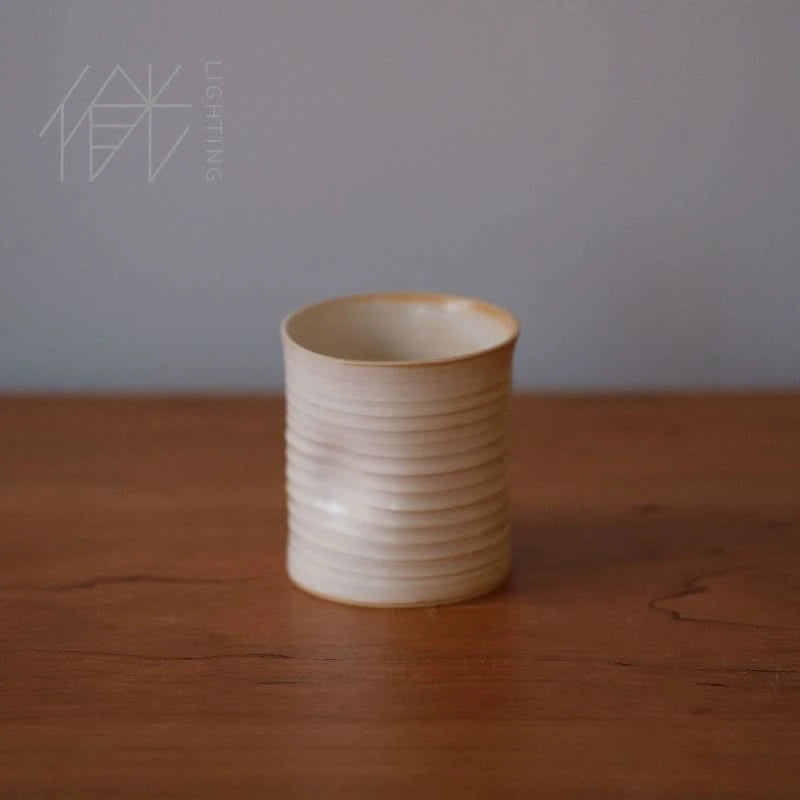 Handmade ceramic dented coffee cup in cream with ribbed texture, on a wooden surface.