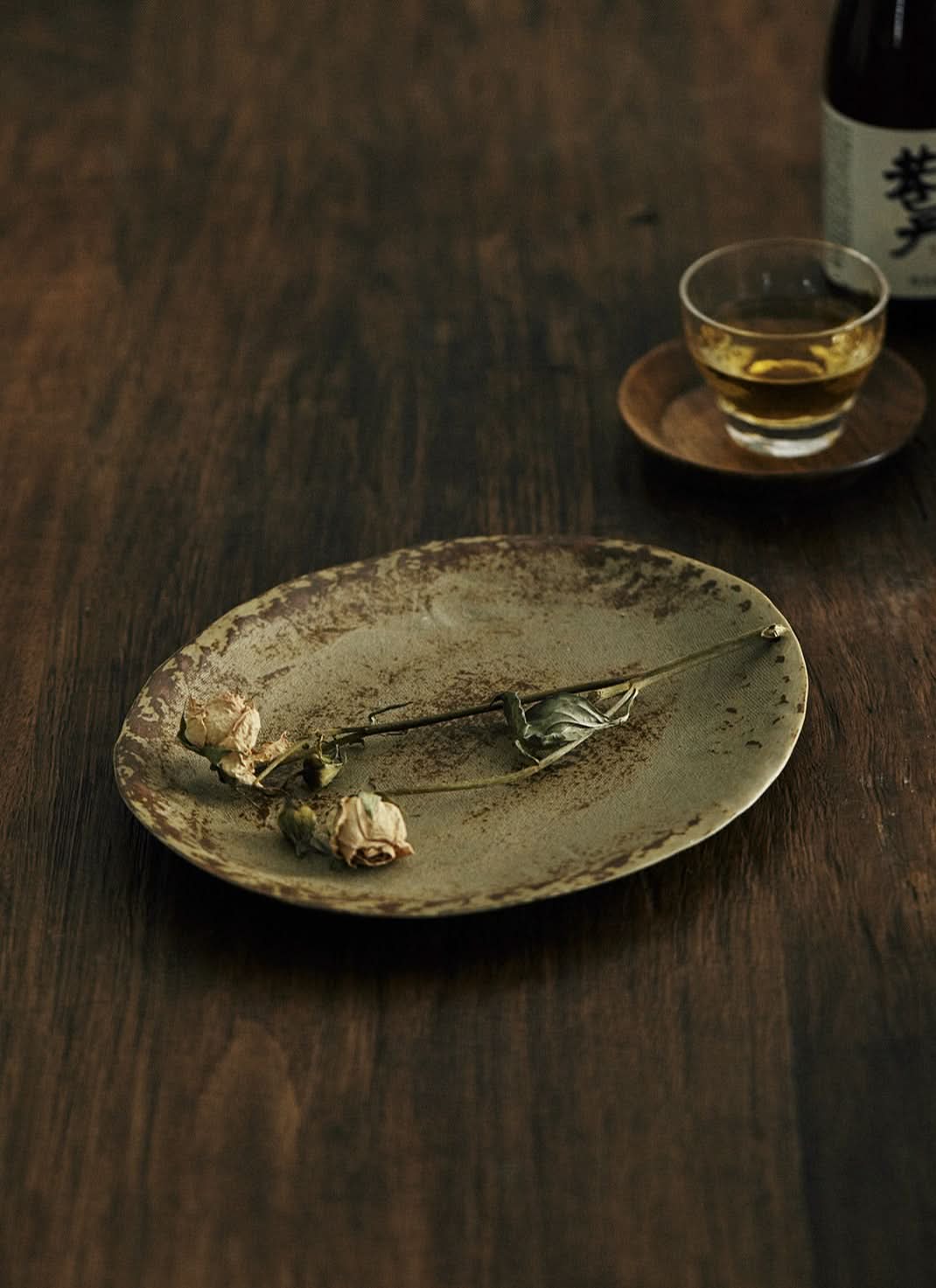 Unglazed ceramic plate with cloth texture, featuring dried roses on a wooden table.
