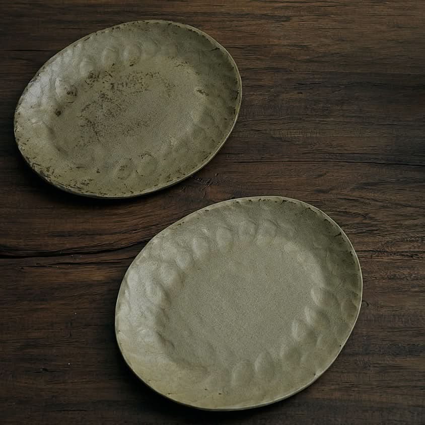 Unglazed ceramic plates with cloth texture in earthy tones on dark wood.