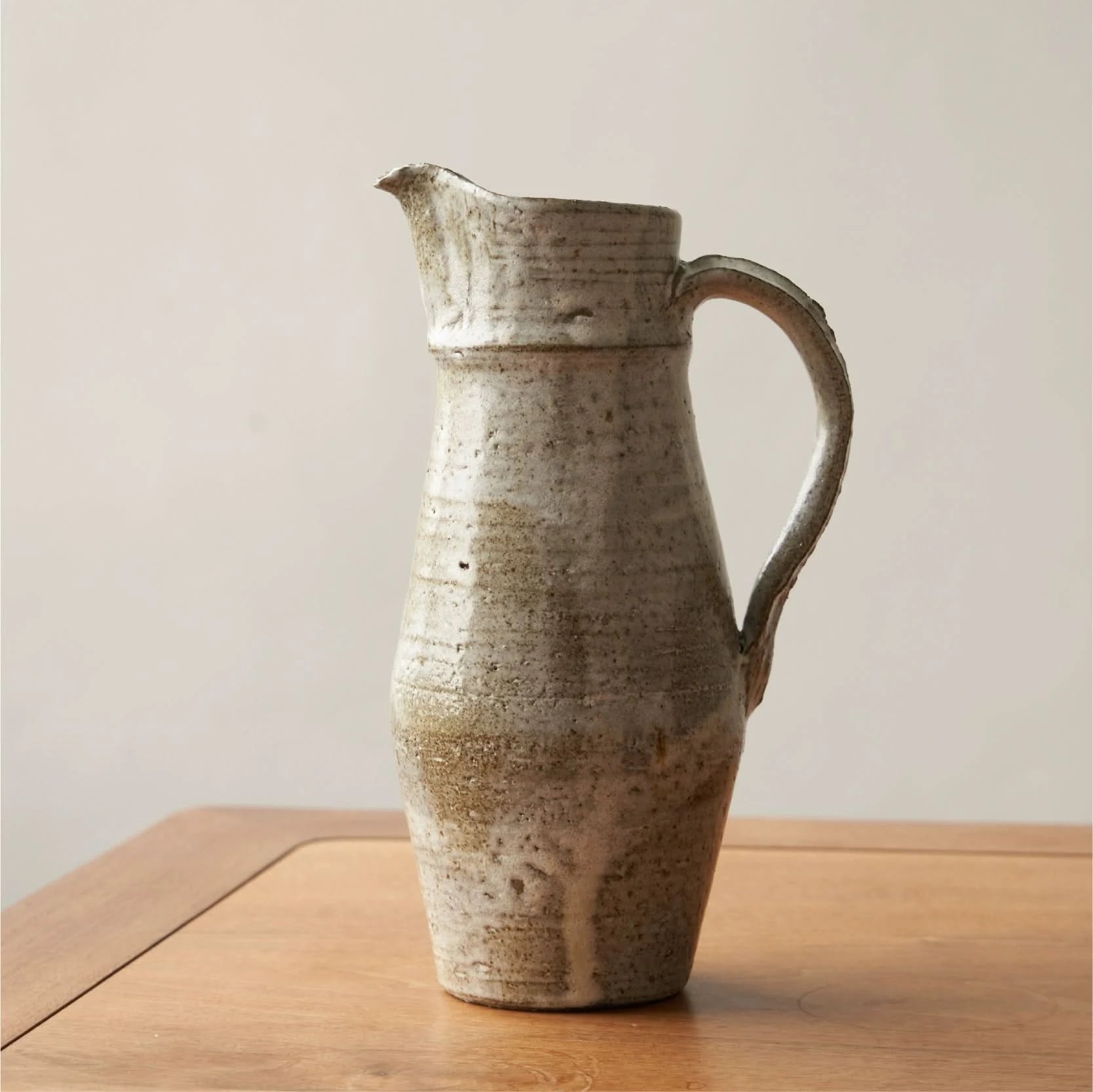 Ceramic jug with rough pottery glaze on a wooden surface. Home decor.