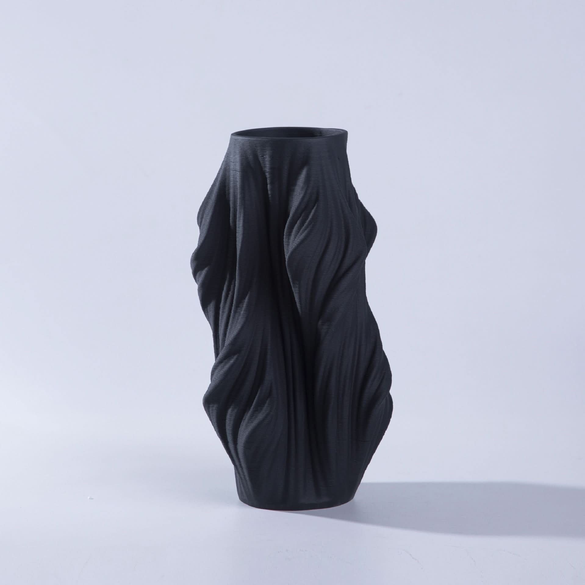 Black 3D printed ceramic vase with flowing, textured design on a white background.
