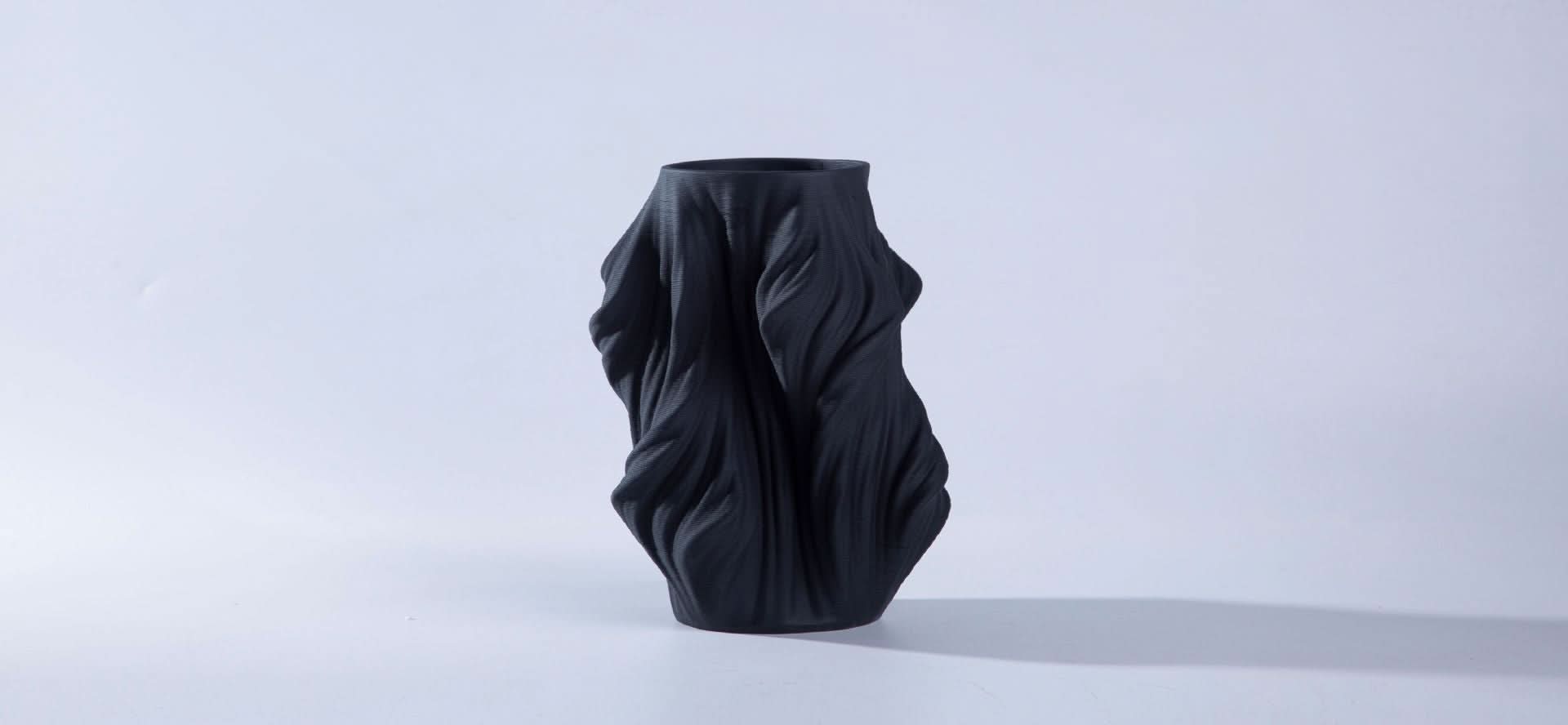 Textured black 3D printed ceramic vase with draped fabric effect on white background.