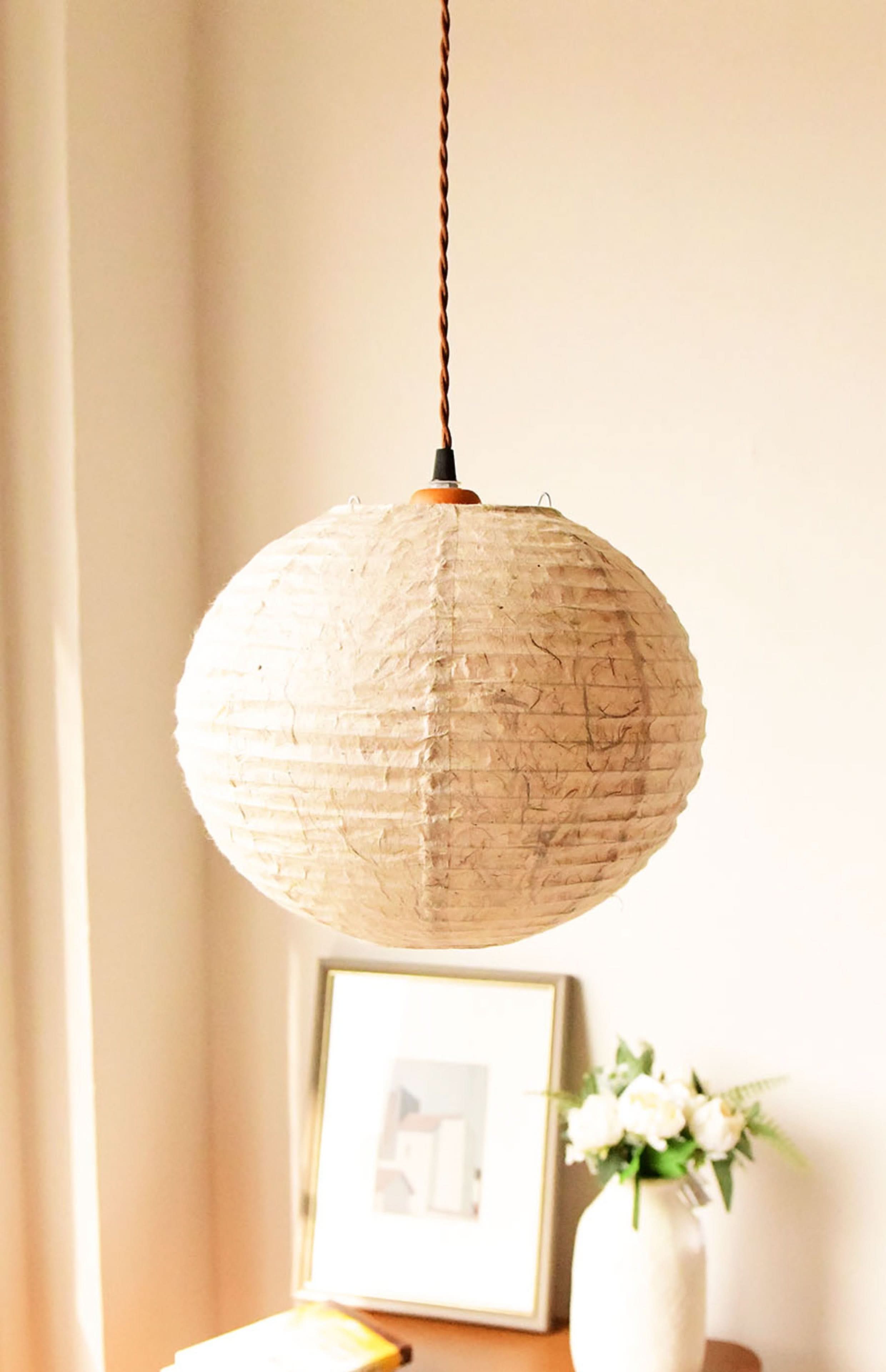 Natural fiber, textured paper lampshade in cream, hanging from a brown cord, home decor accent.