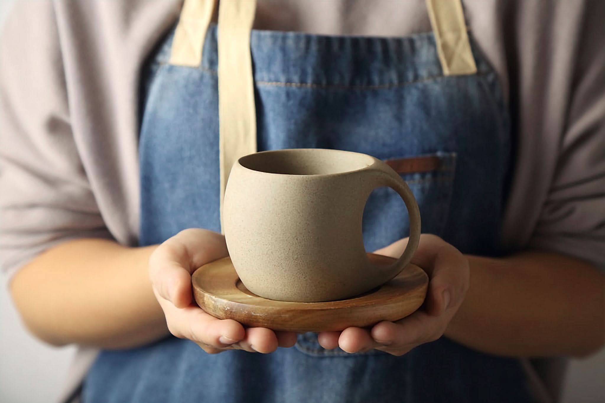 Abstract Ceramic Mug with Arched Handle in earthy tones, held on wooden saucer.