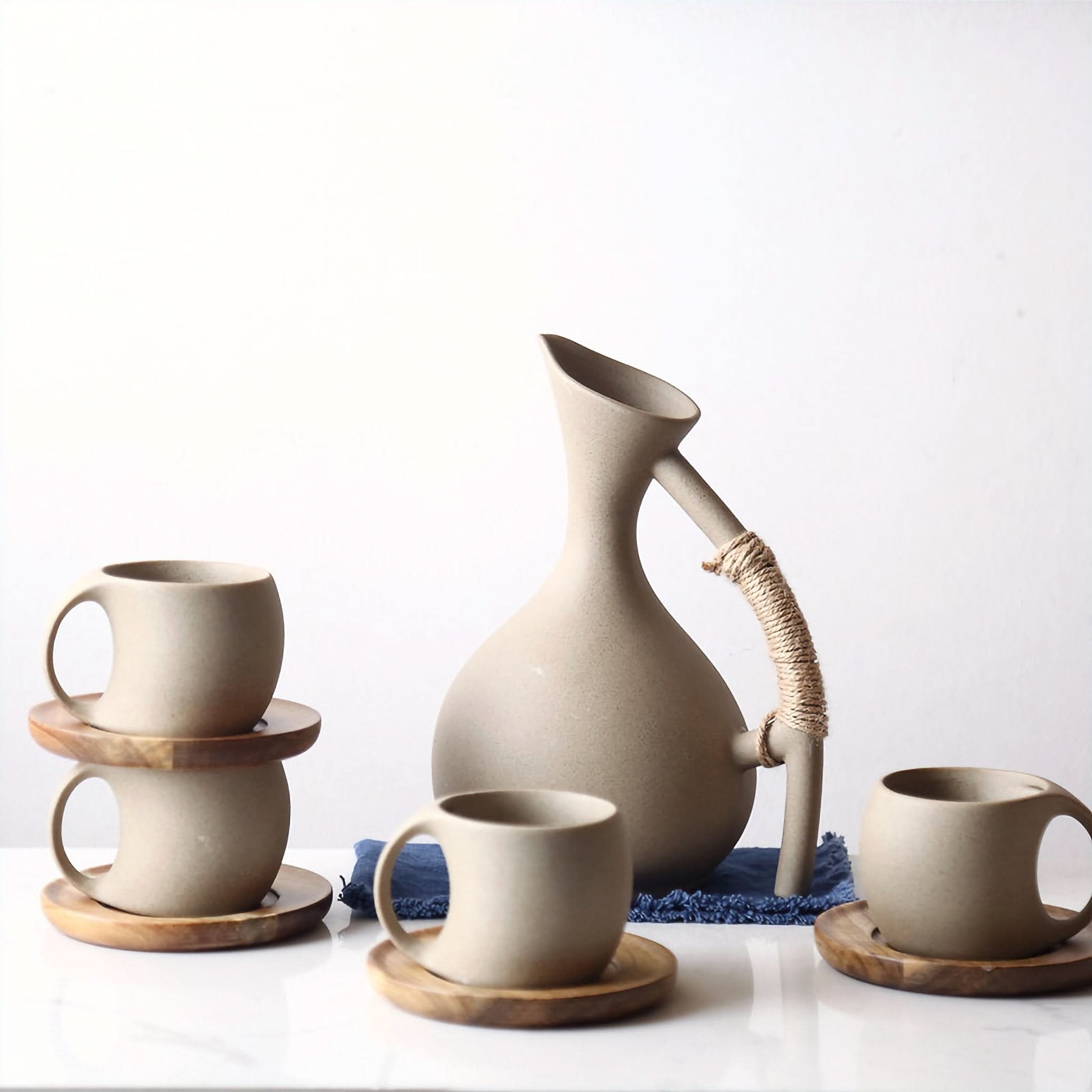 Abstract Ceramic Mugs with Arched Handle: Neutral stoneware mugs and pitcher on wooden coasters, natural home decor.