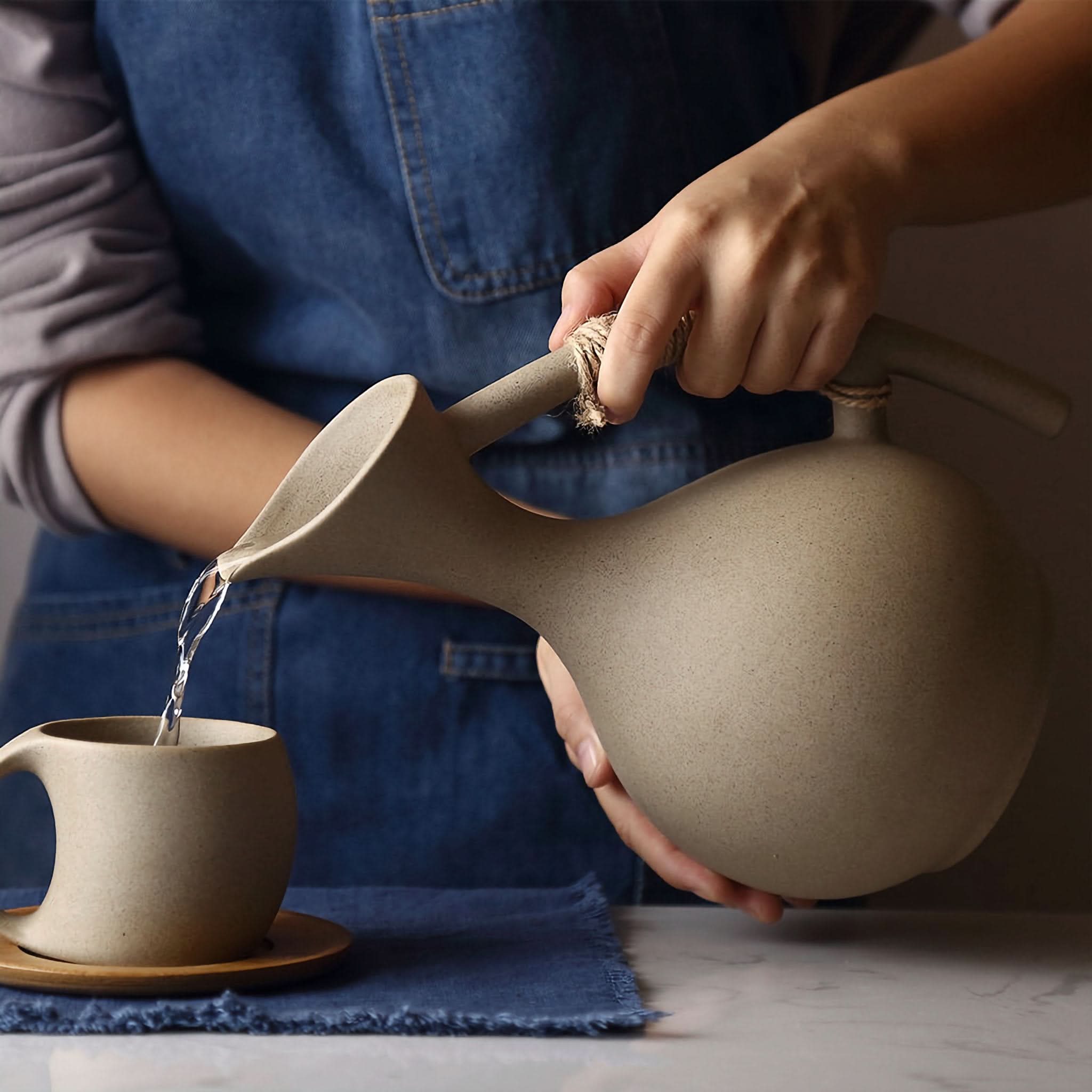 Light tan ceramic mug with arched handle being filled from a matching carafe.
