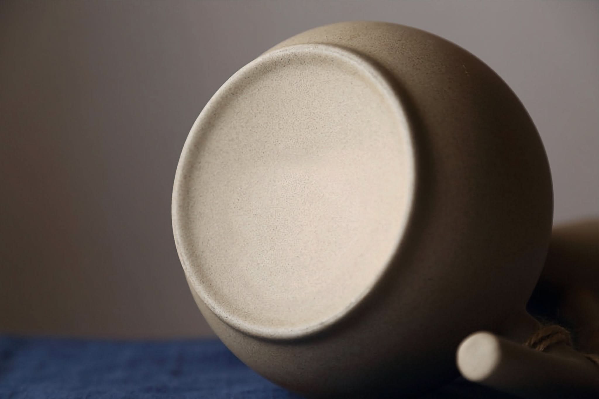 Abstract Ceramic Mug with Arched Handle, neutral tone, textured matte finish, on blue cloth.