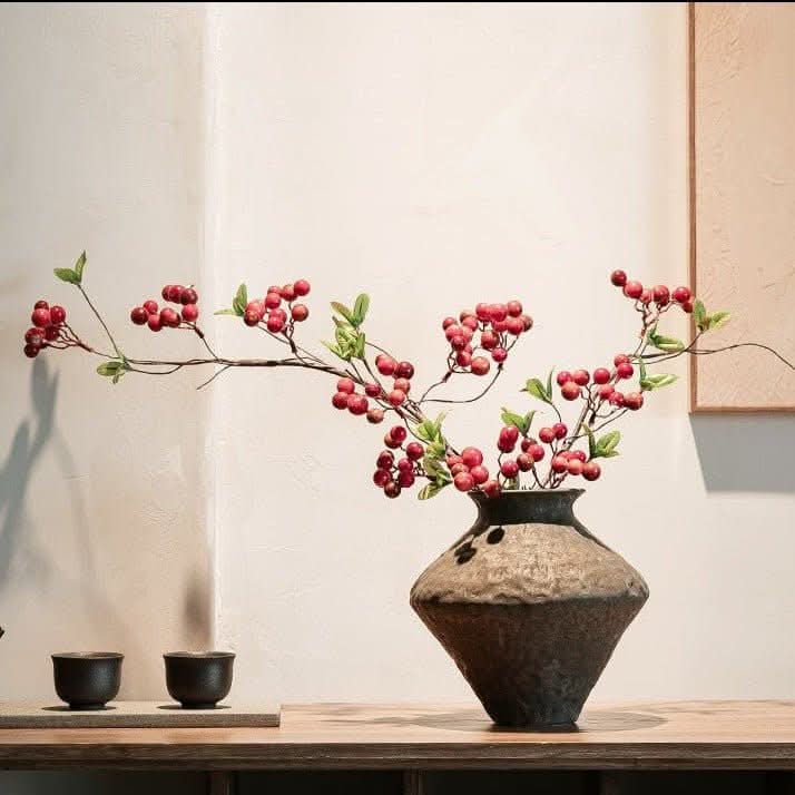 Abstract geometric ceramic vase with hammered texture, holding red berry branches.