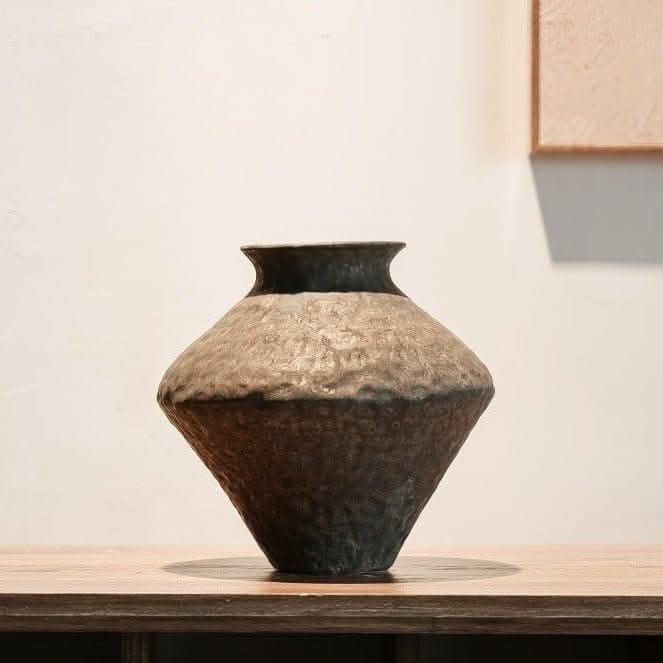 Abstract geometric ceramic vase with hammered texture in earthy tones on a wooden table.