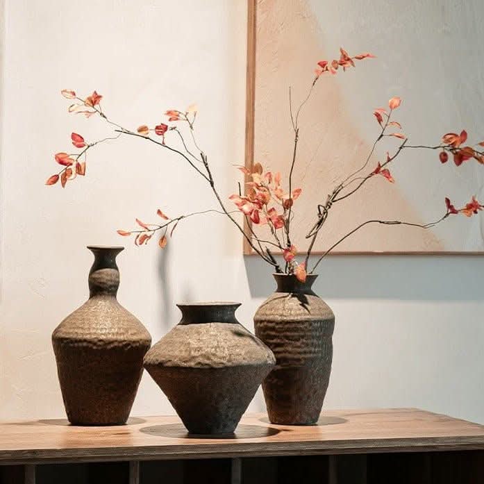 Three hammered geometric ceramic vases, displaying dried orange leaves, on a light-colored wooden surface.
