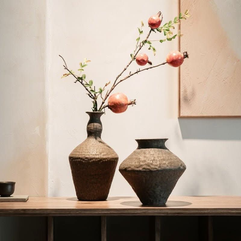 Abstract geometric ceramic vase with hammered texture, holding pomegranate branches on a wooden shelf.
