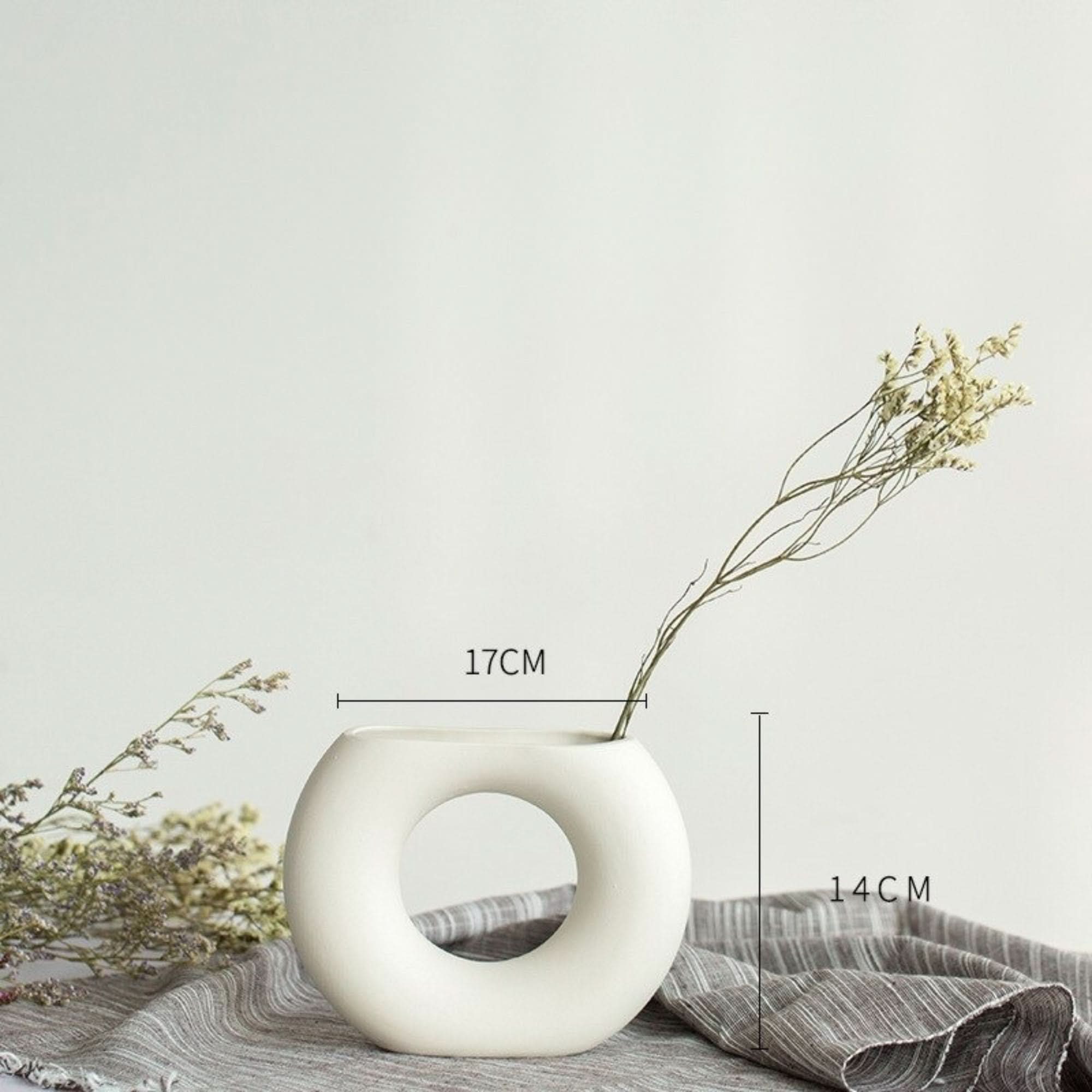 Abstract white flower vase with dried flowers on textured fabric