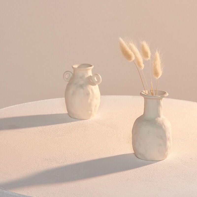 Abstract white ceramic vases on a table, one with fluffy pampas grass.