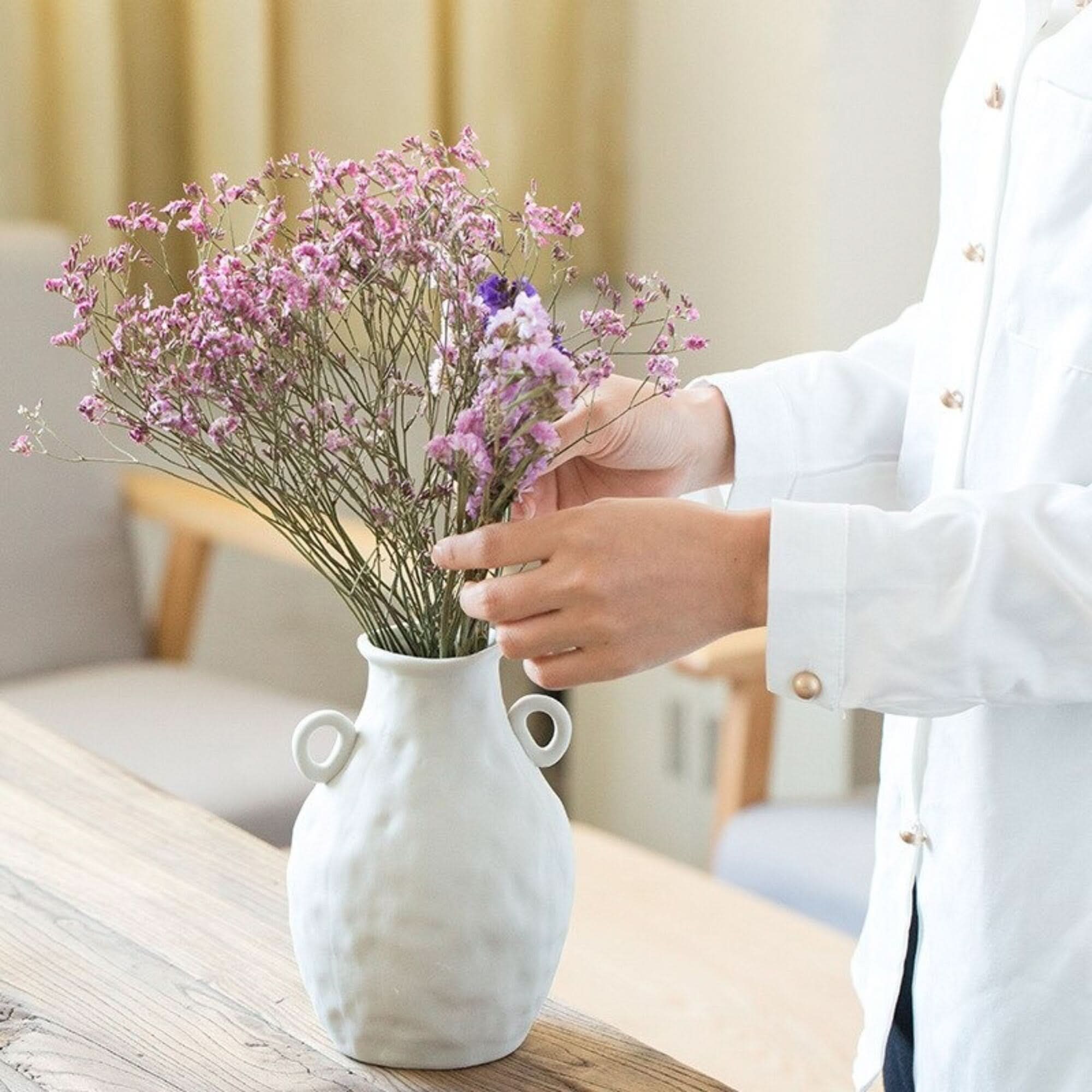 Abstract White Flower Vase with dried pink flowers on wooden table.