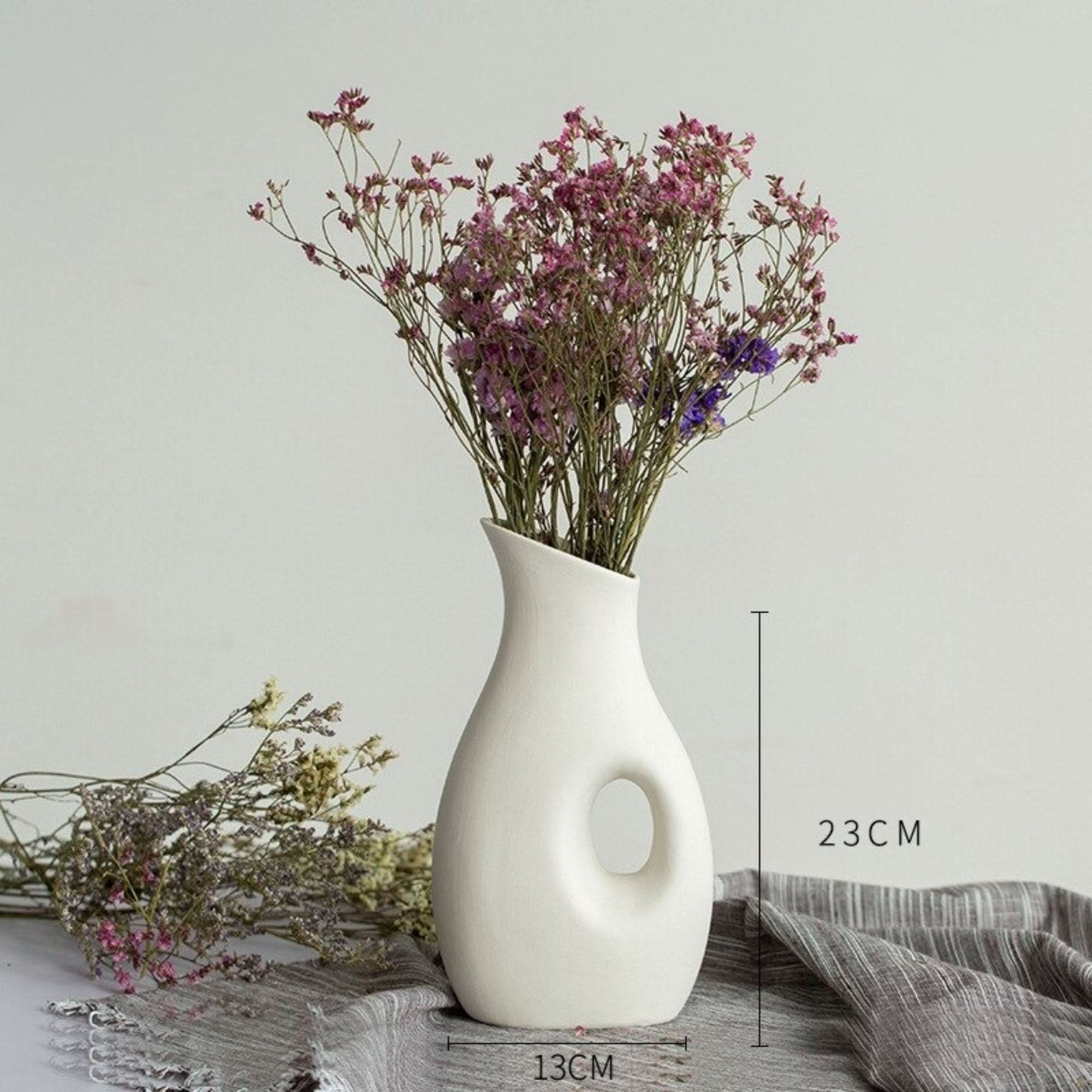 Abstract white vase with dried flowers on gray linen. Decorative minimalist vase.