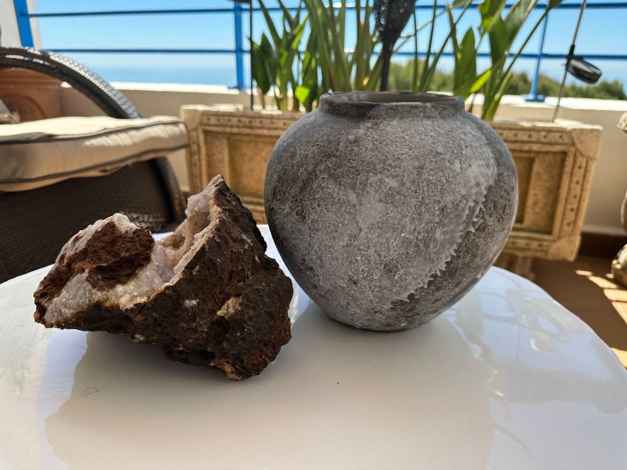 Antique Effect Ceramic Vase: Grey textured stoneware vase on a white surface with rock and greenery.