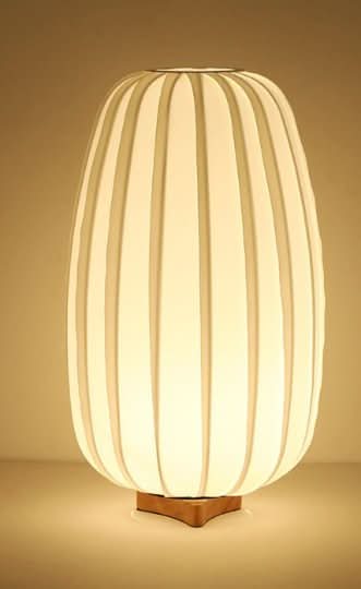 Japandi Table Lamp With Oval Shape: White ribbed shade on wood base, softly lit.