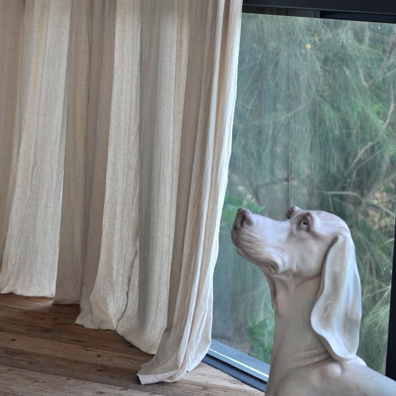 Cream linen curtains with textured weave, beside a window and a white dog statue.