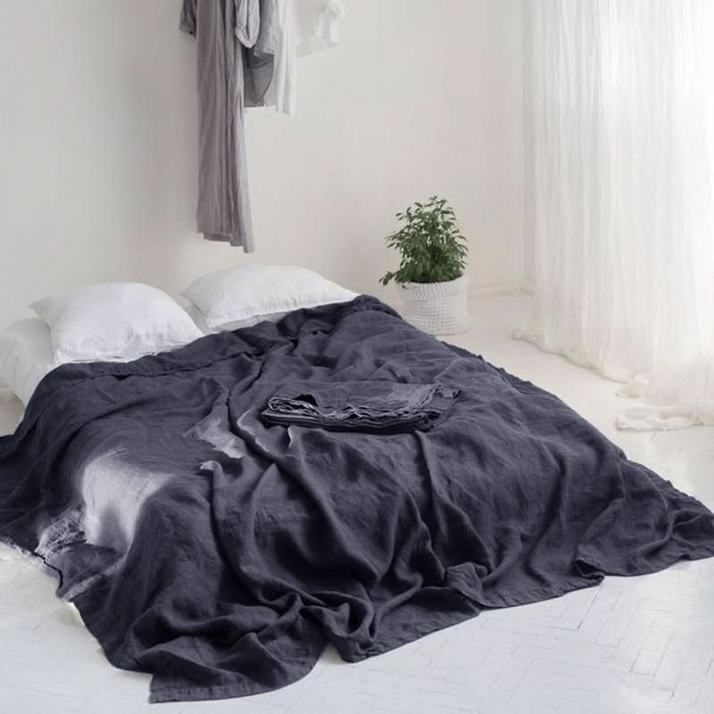 Dark gray linen bed sheets with white pillows on a bed, styled in a bright, airy bedroom.