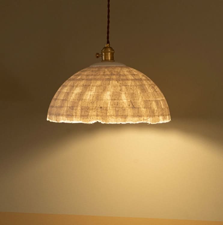 Textured paper mache lamp shade with brass accents, casting warm light.