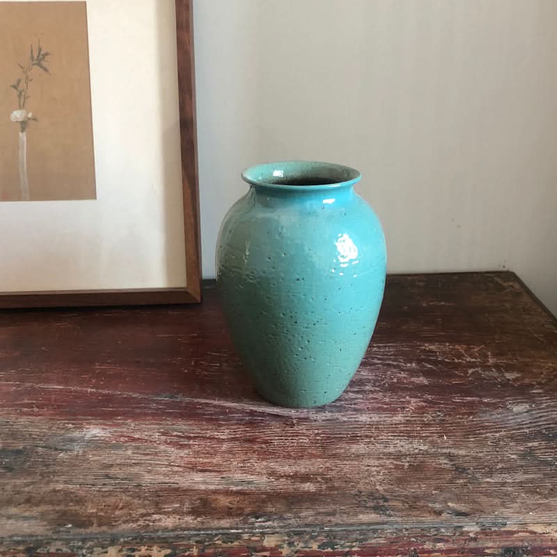 Turquoise speckled ceramic vase for flowers, displayed on a wooden table.