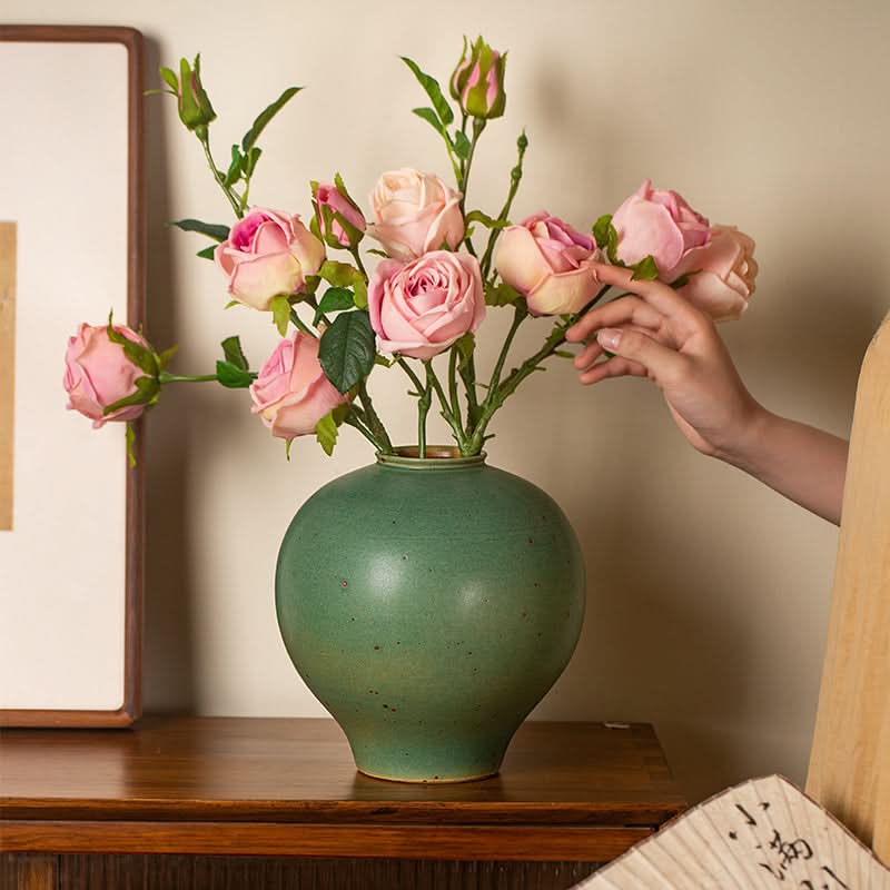 Sage green round vase with pink roses, on a wooden table. Home decor.