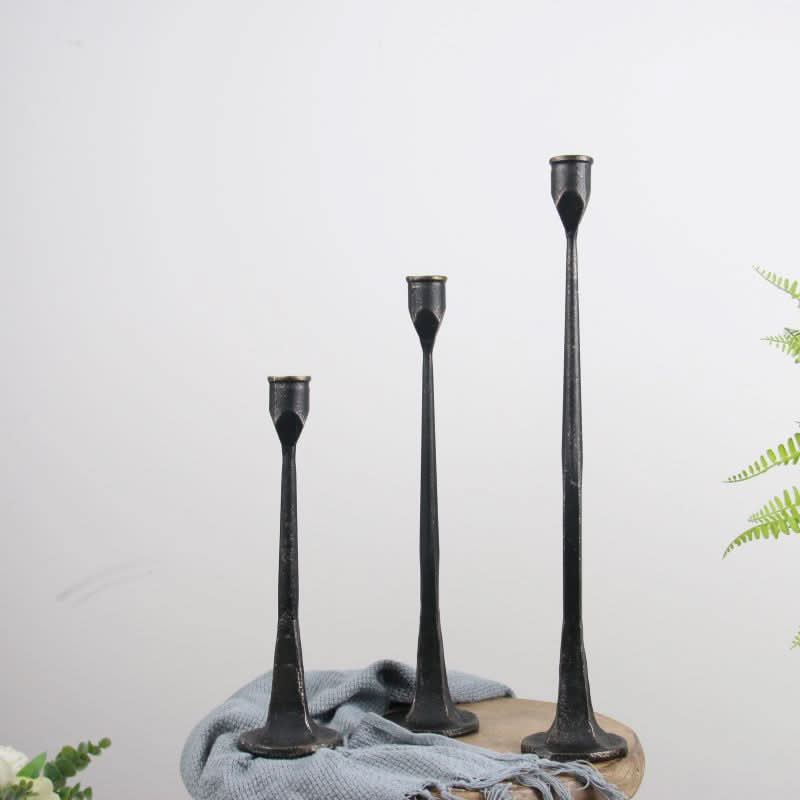 Three black iron candle holders of varying heights on a table with a blue cloth.