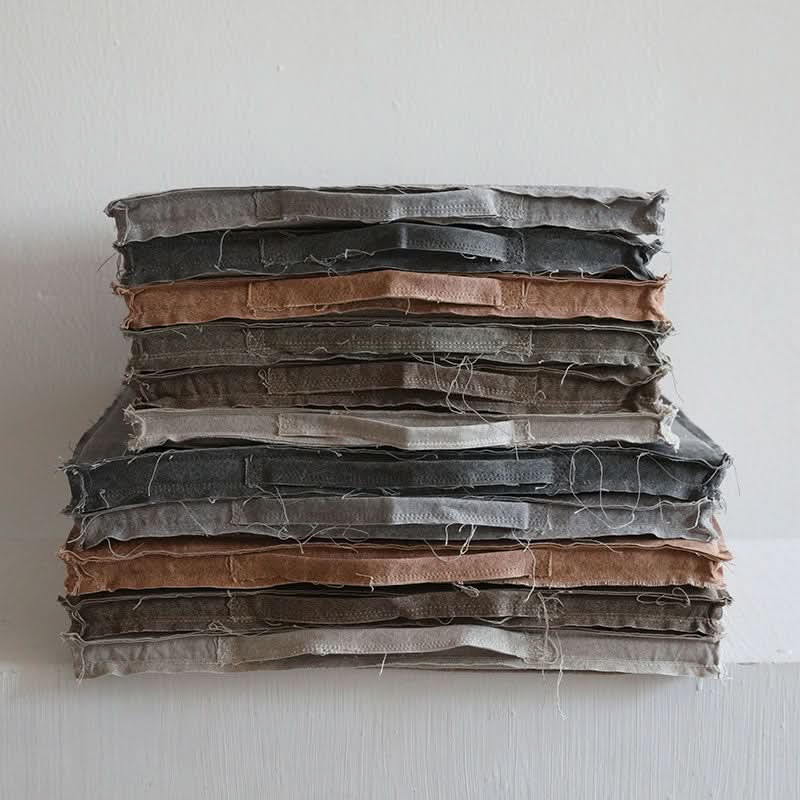 Stack of customizable distressed linen cushion covers in muted grey and rust tones.