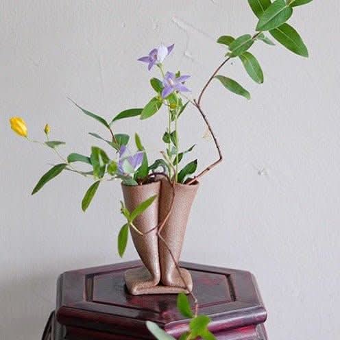 Bent tube textured rough pottery ceramic vase imported from Japan with purple and yellow flowers.