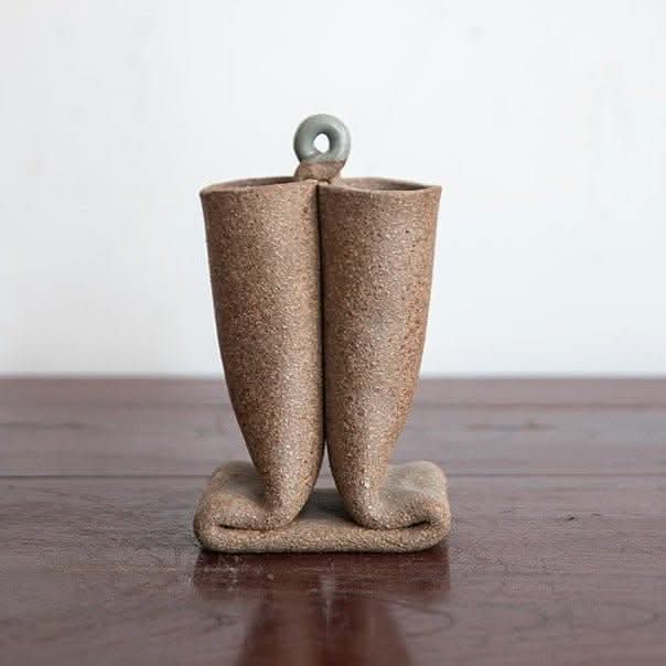 Bent tube textured rough pottery ceramic vase imported from Japan on wooden table.