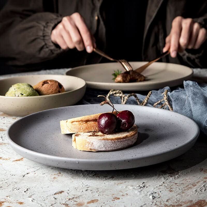 Grey ceramic Nordic plate with bread & cherries, part of all-season tableware.