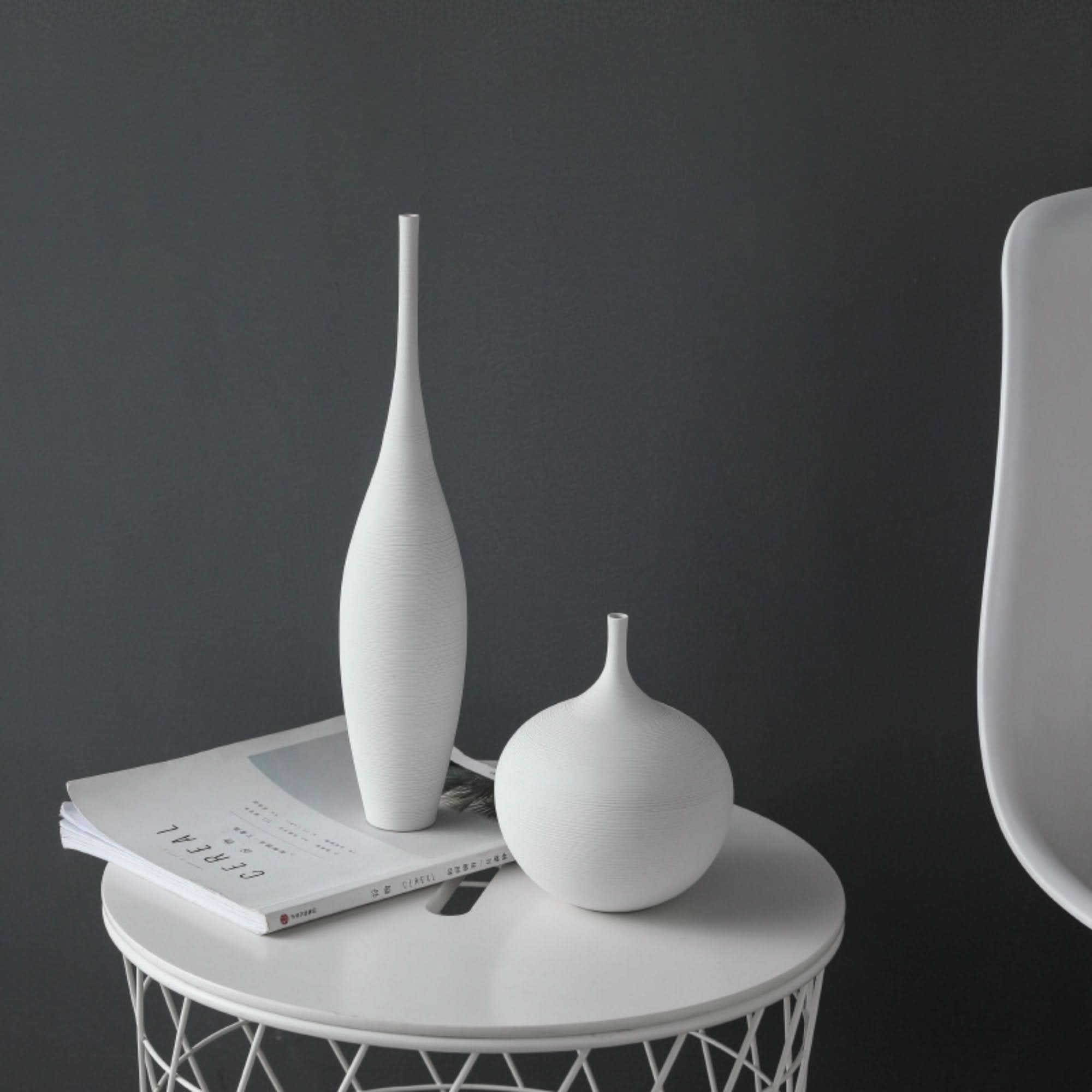 Two white ceramic vases, one tall and slender, the other round and bulbous, on a white table.