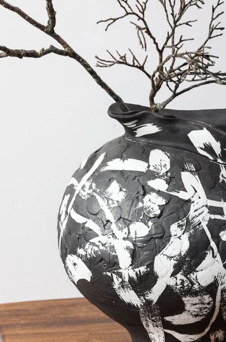 Black irregular wabi-sabi ceramic vase with white brushed effects, featuring branches on a wooden surface.
