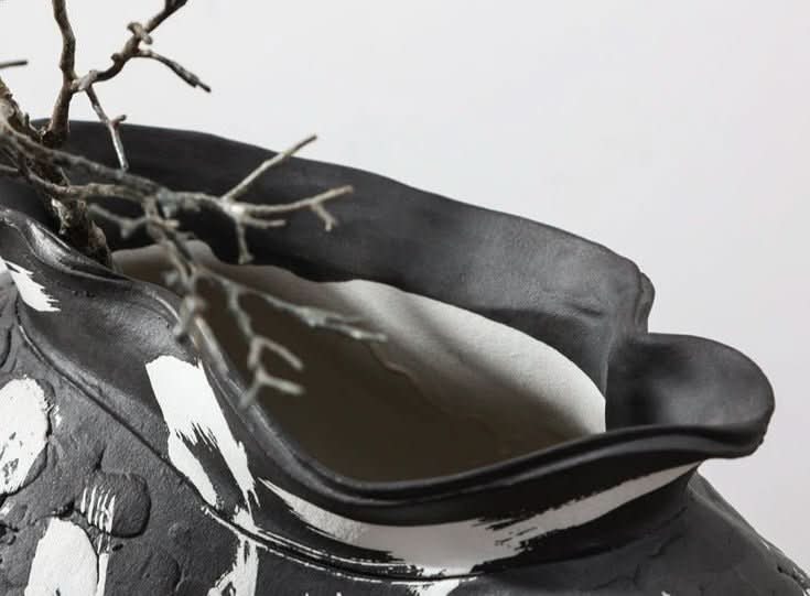 Black irregular wabi-sabi ceramic vase with white brushed effects, holding dry branches.