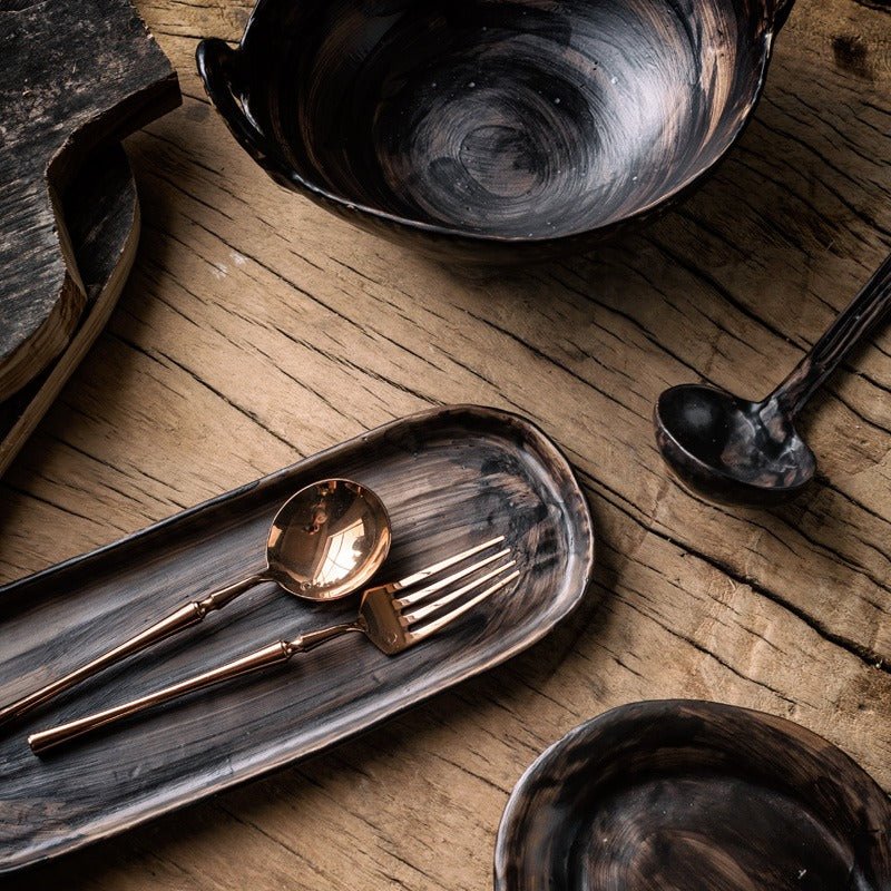 Hand-painted black stoneware tableware set on a rustic wooden table.