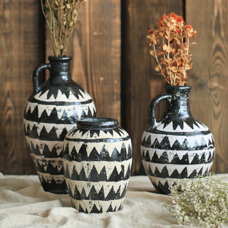 Black and white African motif pottery vase displayed on a light beige surface, with dried flowers.