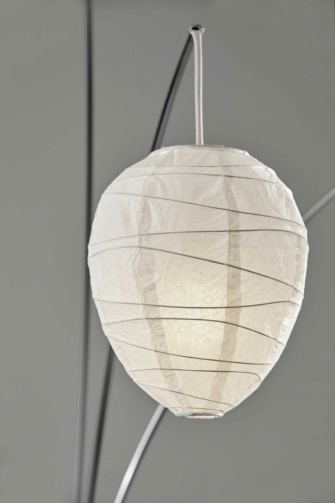 Arc floor lamp with 3 white paper lampshades and dark accents against a gray wall.