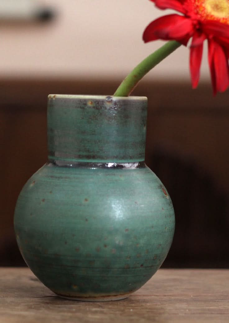Small sage green ceramic vase for flowers, with a red gerbera daisy. Home decor.